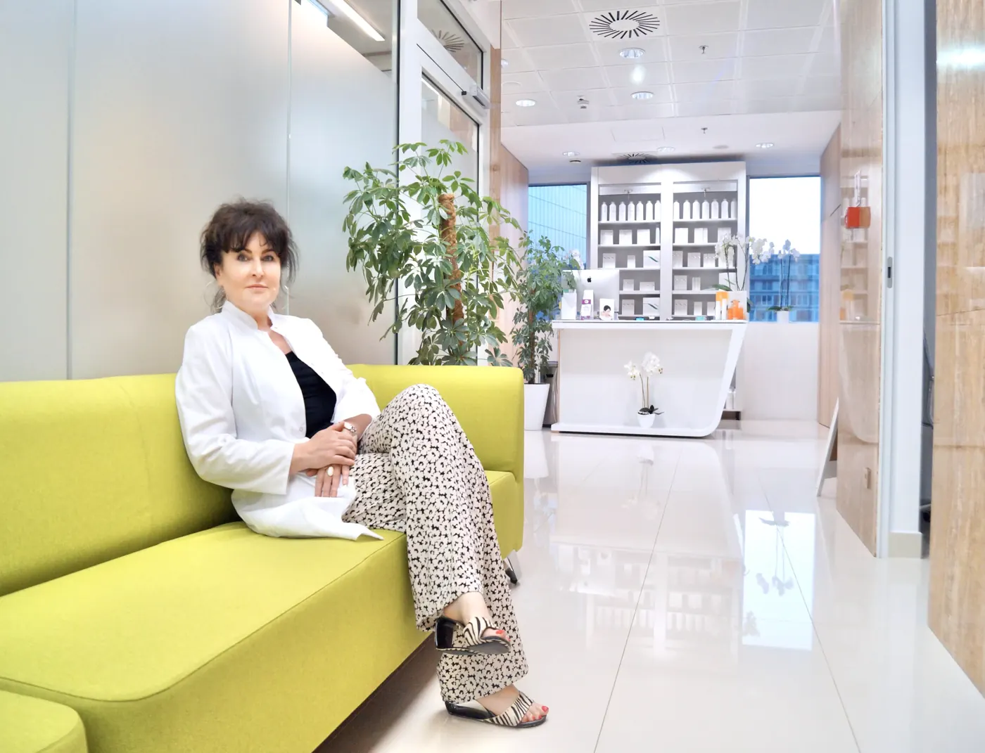 Dr Dorota Nawacka w białym fartuchu siedzi na żółtej kanapie w jasnej poczekalni gabinetu.